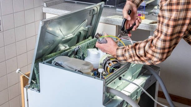 People in technician jobs. Appliance repair technician or handyman works on broken dishwasher in a kittchen. Laborer is changing the heating element.